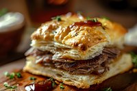 Flaky puff pastry layers filled with tender roast beef slices, garnished with fresh herbs on wooden surface, close up view of gourmet sandwich appetizer.