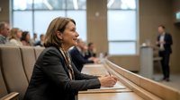 Middle-aged Caucasian businesswoman smiling in modern conference room during corporate meeting with colleagues in background for presentations.