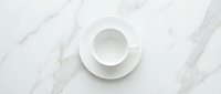 Empty white ceramic cup and saucer on marble surface, overhead view. Minimalist tableware arrangement for beverage, coffee, or tea service design projects.