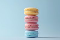 Stack of colorful French macarons in pastel yellow, pink and blue shades on light blue background, sweet dessert cookies with creamy filling for cafe menu.