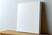 Blank white canvas mockup on wooden table against light wall, ready for artwork presentation. Professional gallery wrapped stretched canvas for painting.