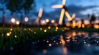 Windmill silhouette at dusk with bokeh lights reflecting in water puddle, green grass in foreground creates dreamy atmospheric landscape for environmental themes.