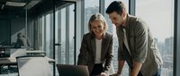 Professional business colleagues collaborating on laptop in modern office with city skyline view during productive meeting session.