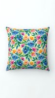 Colorful floral throw pillow with vibrant blue, pink, yellow, and orange blooms scattered across green foliage on white background. Perfect for home decor.