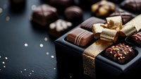 Luxury dark chocolate pralines in elegant black gift box with golden ribbon bow on dark background, selective focus on gourmet confectionery assortment.