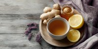 Herbal tea with ginger, honey, and lemon on wooden tray, accompanied by lavender sprigs and fabric napkin on rustic table.