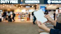 Person holding blank white box in airport duty free shop with cosmetics store and blurred travelers in background, retail shopping and travel concept.