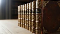 Row of antique leather-bound books with ornate gold decorative patterns and embossed spines arranged on wooden shelf for library or study decor.