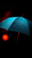 Turquoise umbrella covered in raindrops against dark background with red bokeh light effect, creating dramatic contrast and moody atmosphere.