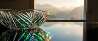 Crystal cut glass bowl on reflective surface with golden sunset and mountain landscape through window, elegant home decor accent.