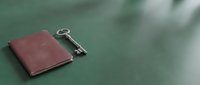 Burgundy leather journal notebook with vintage skeleton key on green surface, symbolizing secrets, access, and discovery for editorial and conceptual projects.