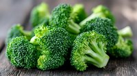Fresh raw broccoli florets on dark wooden background, macro view of green vegetables. Natural organic produce for healthy eating and cooking.