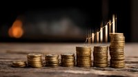Growing stacks of gold coins with upward trending graph in background, symbolizing financial growth and investment success on wooden surface.
