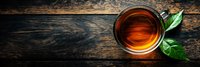 Cup of aromatic black tea with fresh green leaves on dark rustic wooden background, panoramic banner layout with copy space for text.