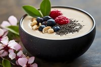 Healthy smoothie bowl with fresh berries, hazelnuts and chia seeds garnished with pink blossom and green leaves, served in black ceramic bowl. Perfect for breakfast.