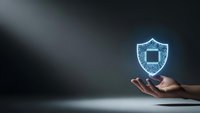 Hand holding glowing digital shield icon representing cybersecurity protection and data safety in modern technology environment.