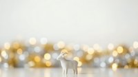 Isolated white goat figurine standing against soft golden and silver bokeh lights, perfect for holiday designs, greeting cards, festive backgrounds, and seasonal marketing materials.
