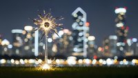 Sparkler burning bright against blurred city skyline at night creating magical bokeh lights celebration atmosphere for holidays and special events.