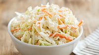 Fresh coleslaw with shredded cabbage and carrots in white ceramic bowl on wooden table, classic side dish for summer barbecue and picnics.