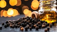 Black peppercorns scattered on dark surface with honey jar and golden bokeh lights in background, moody food photography composition for culinary designs.