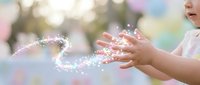 Child hands reaching for magical sparkles and glitter in dreamy outdoor setting with soft bokeh background creating enchanting fairy tale atmosphere.