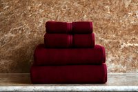 Stack of soft burgundy cotton towels on marble surface against textured stone wall, cozy bathroom decor concept.