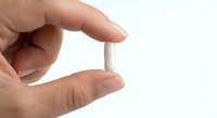 Hand holding white pill tablet between fingers on clean background for medical healthcare pharmaceutical concept.