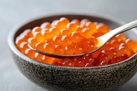 Fresh red caviar in ceramic bowl with spoon, bright orange salmon roe close up on gray background, luxury seafood delicacy for gourmet appetizer.