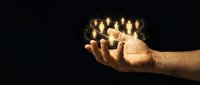 Hand holding glowing candles against dark background, symbolizing hope, spirituality, and remembrance for memorial, religious, or wellness design projects.