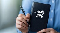 Person holding black notebook with Goals 2026 text written on cover. Business planning and future aspirations concept shown through close-up of hands and planner.