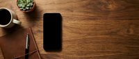 Smartphone with blank black screen on wooden desk workspace with coffee cup, succulent plant and eyeglasses for business mockup and technology concepts.