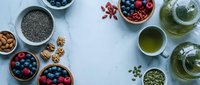 Healthy superfood ingredients with berries, nuts, seeds and green tea arranged on light blue background for nutritious breakfast or snack preparation.