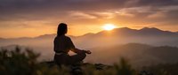 Woman meditating in lotus position on mountain peak at golden sunset with layered hills and warm sky creating peaceful mindfulness scene for wellness content.