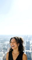 Young woman with curly dark hair and Latin ethnicity smiling joyfully against urban skyline backdrop from high-rise vantage point. Lifestyle and happiness concept.