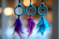 Three colorful dreamcatchers with purple and blue feathers hanging against blurred bokeh background, traditional native american spiritual amulets.
