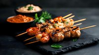 Grilled shrimp skewers with spices and herbs served on black stone plate with creamy dipping sauces, garnished with fresh parsley leaves in dark moody setting.