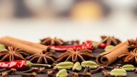 Aromatic winter spices including cinnamon sticks, star anise, cardamom pods and dried chili peppers arranged on wooden surface for seasonal cooking and baking.