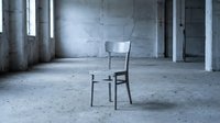 Wooden chair sitting alone in empty concrete industrial loft space with natural light from windows, suitable for minimalist design and architectural photography projects.
