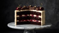 Decadent chocolate cherry layer cake with white cream frosting and fresh cherries on marble stand against dark background for dessert menu.