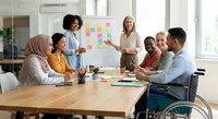 Diverse business team collaborating in modern office meeting room with sticky notes on whiteboard during strategic planning session.