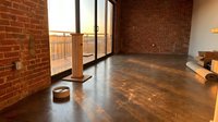 Empty loft interior with exposed red brick walls, polished concrete flooring, and large windows overlooking balcony, suitable for real estate, industrial design, and commercial space showcasing.