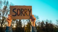 Person holding cardboard sign with sorry message outdoors against blue sky background for apology and forgiveness concepts in communication.