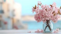 Delicate pink cherry blossoms arranged in glass mason jar against soft pastel blue background, creating romantic spring atmosphere with fallen petals on white surface.