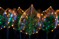 Glowing leaf-shaped light decoration with green tree pattern against dark background, surrounded by similar illuminated ornaments.
