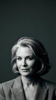 Mature woman with gray and white hair styled in a bob cut, fair complexion, wearing a gray blazer against a dark background. Professional headshot suitable for corporate, business, and executive portraits.