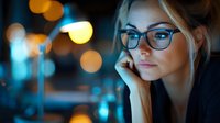 Young blonde woman wearing glasses in moody night lighting with bokeh effect background, contemplative expression, soft focus portrait in blue and orange tones.