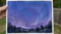 Hand holding watercolor painting of starry night sky with purple blue gradient over silhouetted mountain forest landscape for artistic home decor projects.