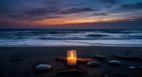 Glowing candle lantern on sandy beach at twilight with ocean waves and colorful sunset sky creating peaceful meditation atmosphere for relaxation.