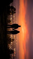 Silhouettes of two people standing on beach at sunset with golden bokeh lights and warm orange sky, suitable for travel, lifestyle, and romantic concepts.