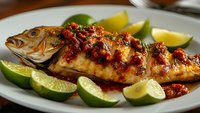 Grilled whole fish with spicy chili sauce and fresh lime wedges on white plate. Perfectly cooked seafood dish ready for restaurant menu or cooking blog.